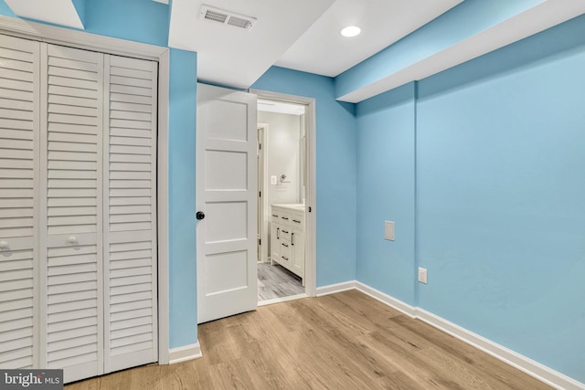 unfurnished bedroom featuring connected bathroom, light hardwood / wood-style flooring, and a closet