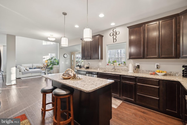 kitchen featuring decorative light fixtures, a center island, stainless steel dishwasher, dark wood-type flooring, and dark brown cabinets