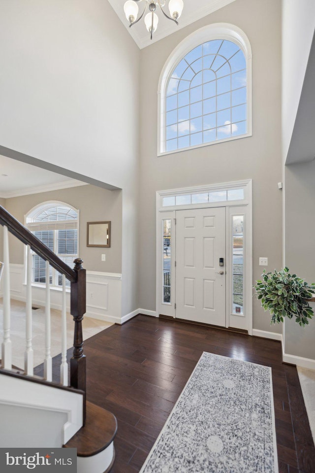 foyer with an inviting chandelier, dark hardwood / wood-style flooring, high vaulted ceiling, and crown molding