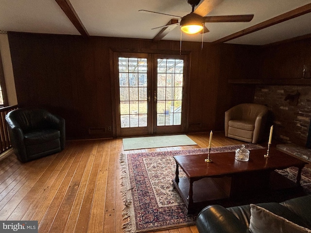 living room featuring ceiling fan, beam ceiling, light hardwood / wood-style floors, and wood walls