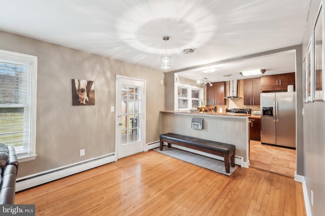 kitchen featuring baseboard heating, dark brown cabinets, stainless steel fridge with ice dispenser, kitchen peninsula, and wall chimney exhaust hood