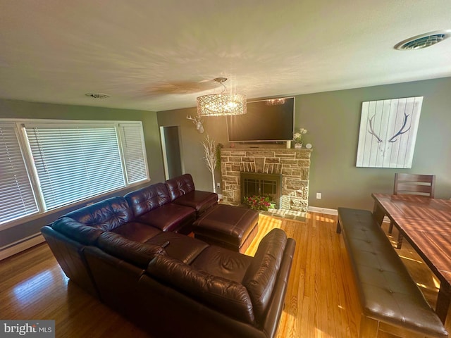 living room with hardwood / wood-style flooring, a stone fireplace, and a notable chandelier