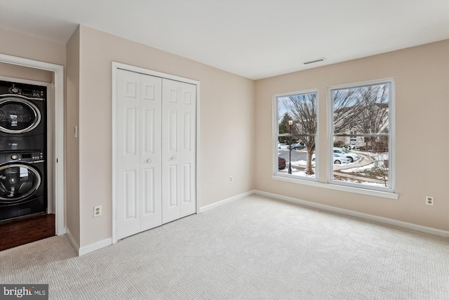 unfurnished bedroom featuring light colored carpet, stacked washer and clothes dryer, and a closet