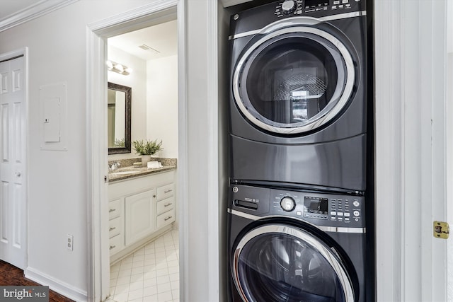 clothes washing area featuring stacked washing maching and dryer, sink, and ornamental molding