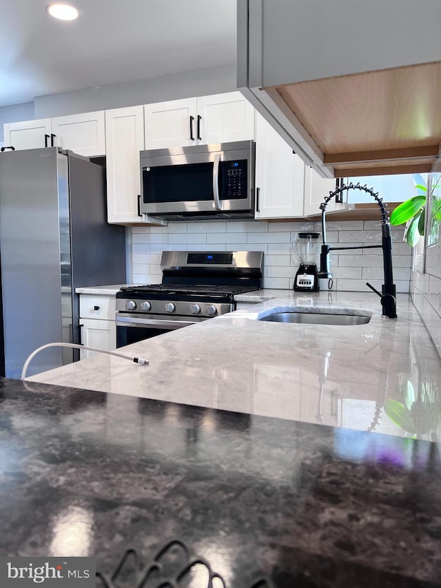 kitchen with light stone countertops, stainless steel appliances, backsplash, white cabinetry, and sink