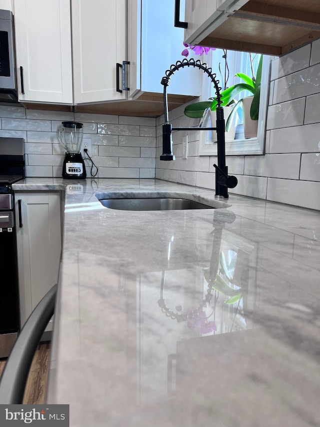 room details with sink, appliances with stainless steel finishes, decorative backsplash, and white cabinetry