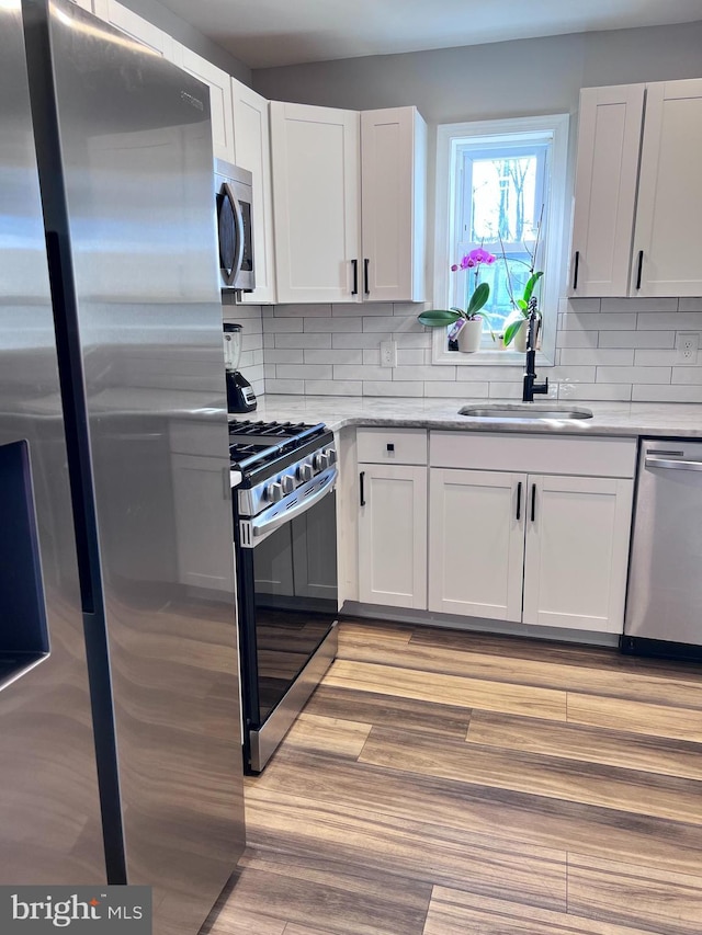 kitchen featuring stainless steel appliances, light hardwood / wood-style floors, decorative backsplash, white cabinetry, and sink