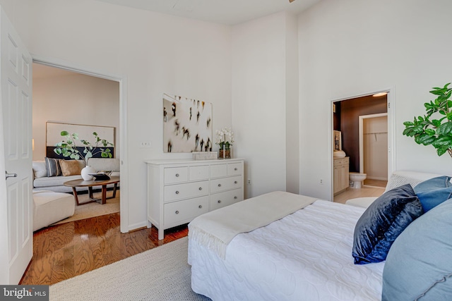 bedroom with ensuite bathroom, light hardwood / wood-style flooring, and a high ceiling