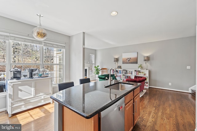 kitchen with dishwasher, dark stone countertops, sink, dark hardwood / wood-style floors, and a center island with sink