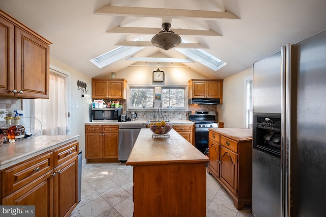 kitchen featuring vaulted ceiling with skylight, a center island, decorative backsplash, and appliances with stainless steel finishes