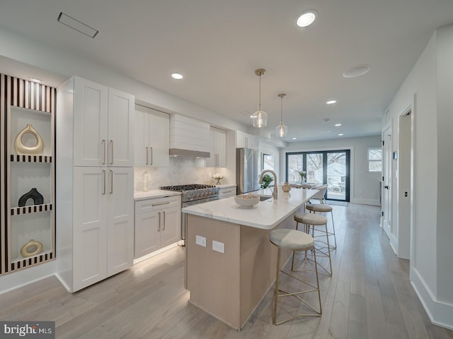 kitchen with white cabinetry, an island with sink, hanging light fixtures, and wall chimney range hood