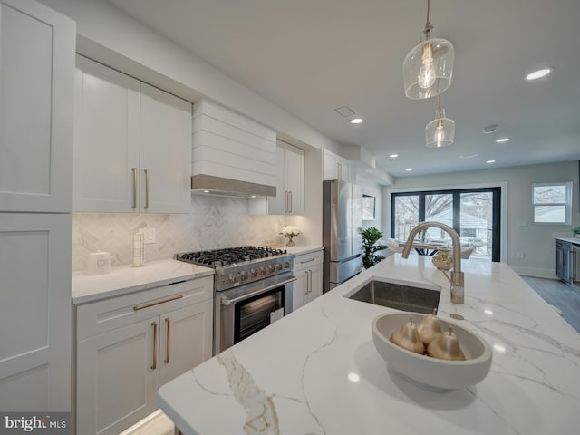 kitchen with appliances with stainless steel finishes, white cabinetry, decorative backsplash, hanging light fixtures, and light stone counters