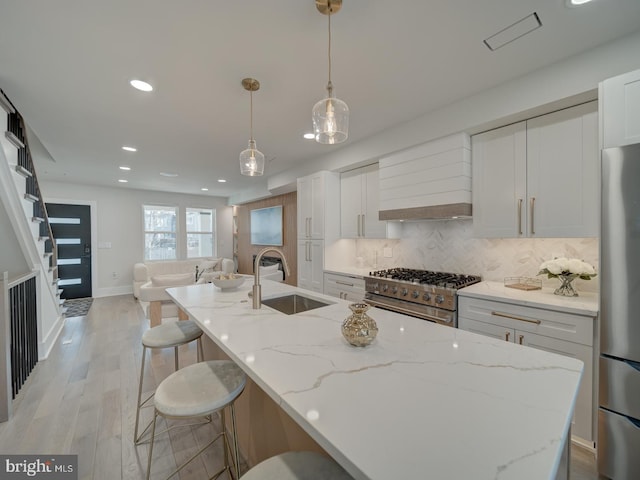 kitchen with sink, white cabinetry, light stone counters, hanging light fixtures, and appliances with stainless steel finishes