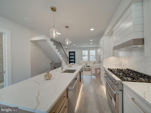 kitchen featuring decorative light fixtures, sink, white cabinets, a kitchen island with sink, and stainless steel appliances