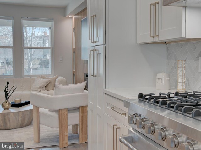 kitchen with stovetop, white cabinets, decorative backsplash, exhaust hood, and light stone countertops