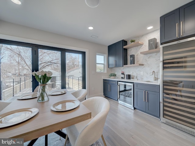 kitchen with sink, wine cooler, light wood-type flooring, and decorative backsplash