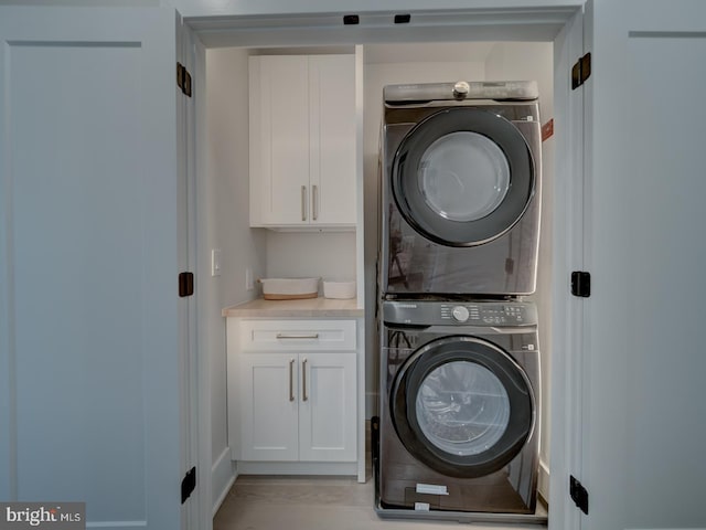 laundry room featuring cabinets, stacked washer / dryer, and light hardwood / wood-style floors