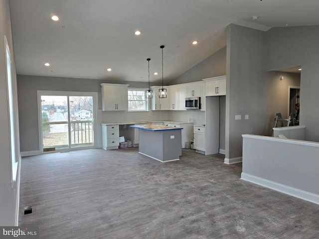 kitchen with stainless steel microwave, open floor plan, white cabinetry, a kitchen island, and wood finished floors