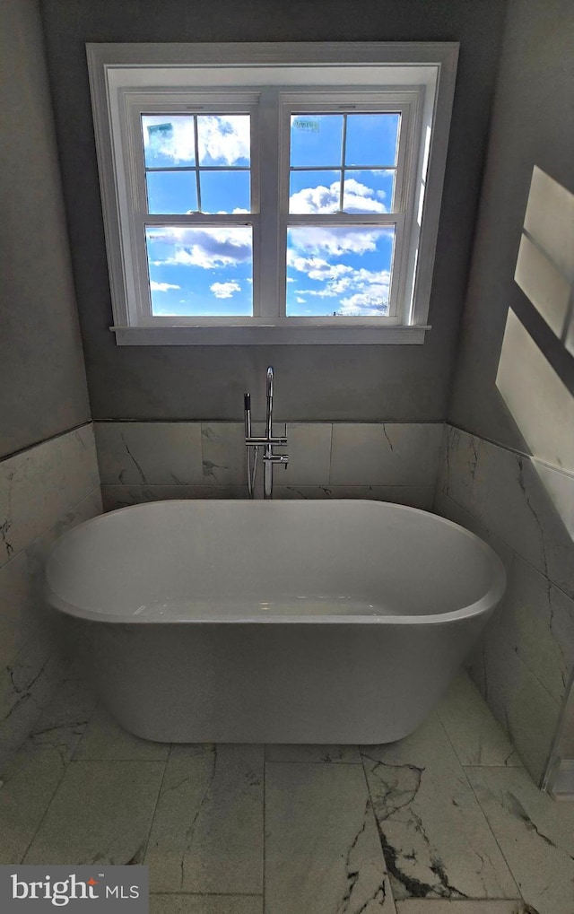 bathroom featuring marble finish floor and a freestanding bath