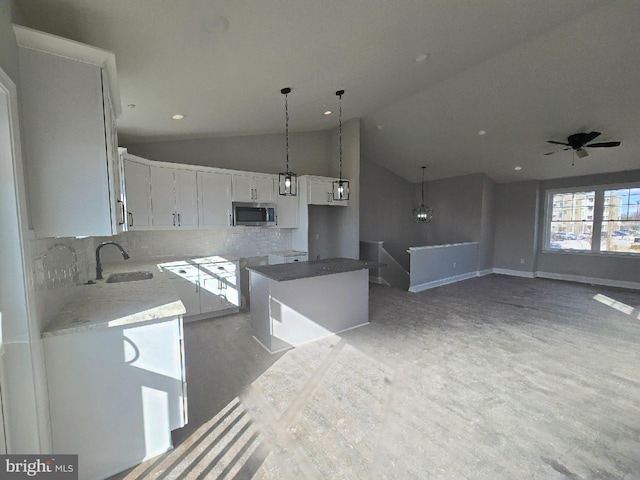 kitchen with tasteful backsplash, white cabinets, stainless steel microwave, vaulted ceiling, and a sink