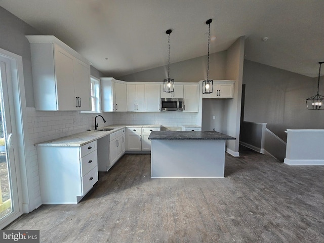 kitchen with a center island, stainless steel microwave, white cabinets, a sink, and wood finished floors