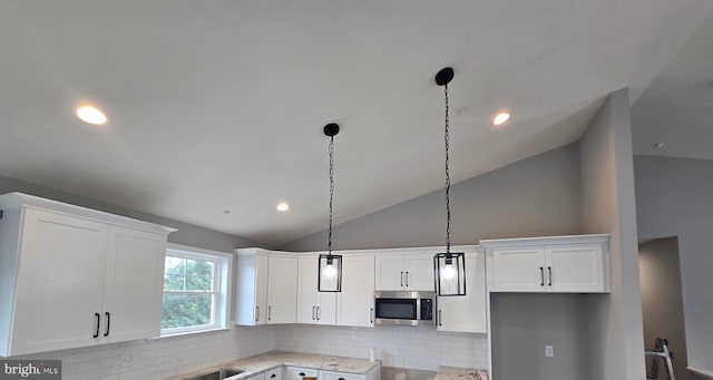 kitchen with hanging light fixtures, stainless steel microwave, white cabinetry, and decorative backsplash