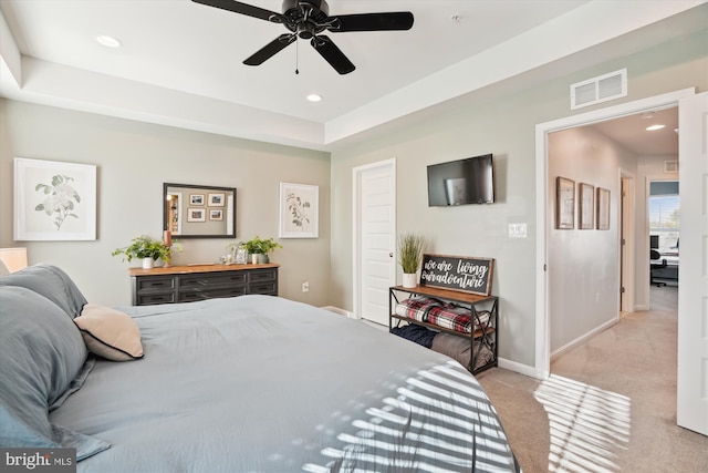 bedroom featuring ceiling fan, light colored carpet, and a tray ceiling