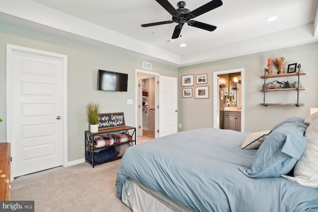 carpeted bedroom featuring ceiling fan, ensuite bathroom, and a tray ceiling