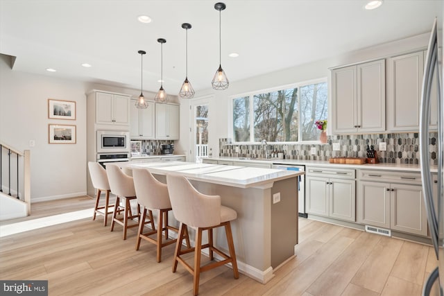 kitchen featuring decorative backsplash, light wood-type flooring, a kitchen island, pendant lighting, and stainless steel appliances