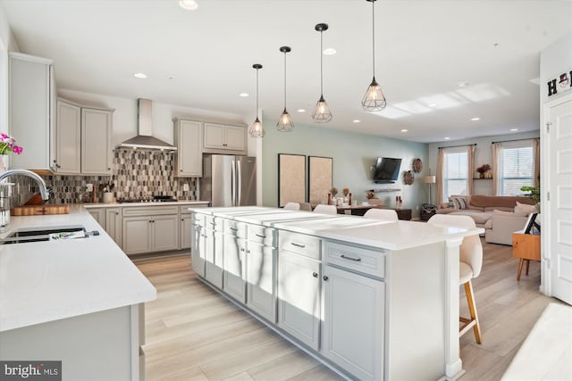 kitchen with a kitchen island, decorative light fixtures, wall chimney range hood, sink, and stainless steel fridge