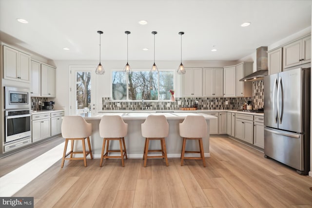 kitchen featuring wall chimney range hood, a kitchen island, backsplash, stainless steel appliances, and a breakfast bar area