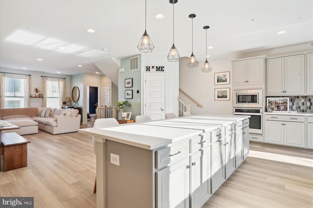 kitchen featuring light hardwood / wood-style flooring, appliances with stainless steel finishes, decorative light fixtures, a kitchen island, and decorative backsplash