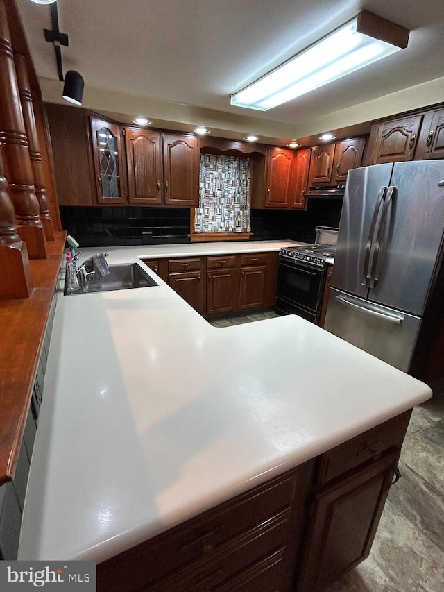 kitchen with black electric range, light countertops, decorative backsplash, freestanding refrigerator, and a sink