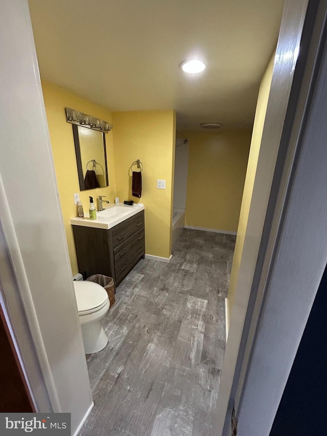 bathroom featuring toilet, vanity, wood finished floors, baseboards, and walk in shower