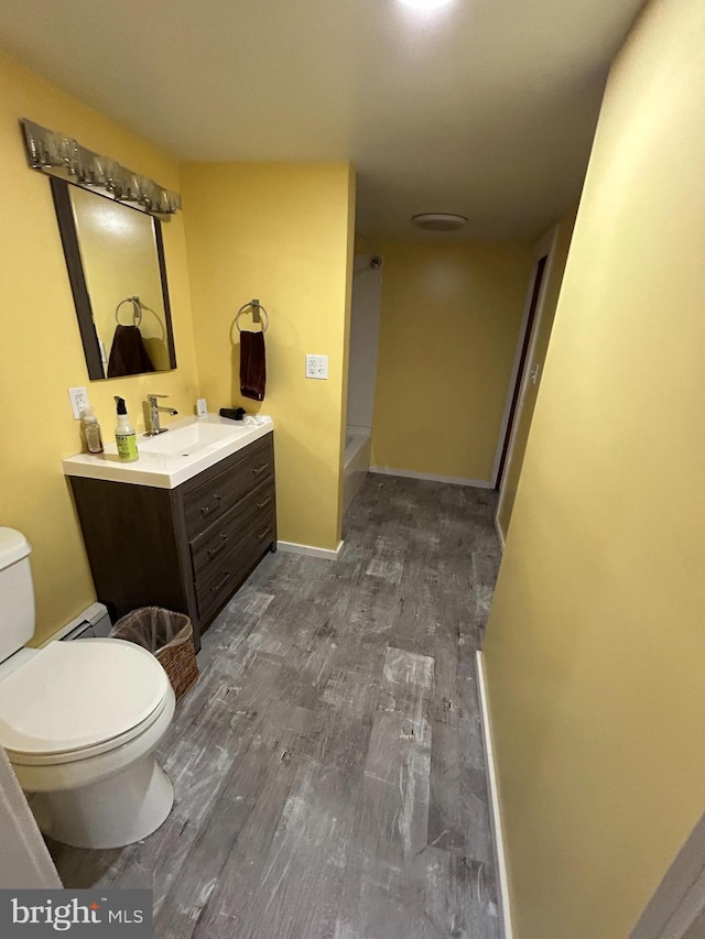 full bath featuring toilet, a baseboard heating unit, wood finished floors, vanity, and walk in shower