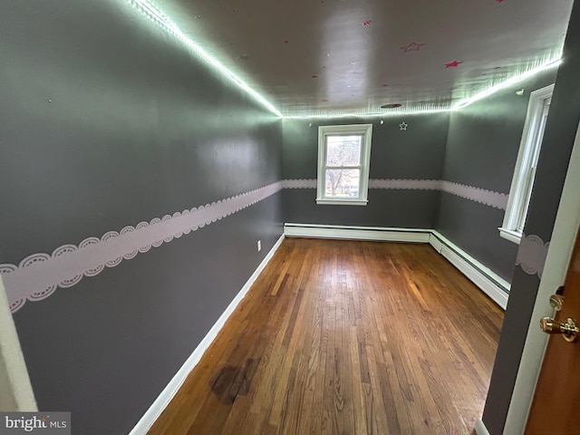 empty room with a baseboard radiator, baseboards, and wood finished floors