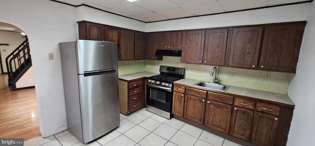 kitchen featuring sink, light tile patterned flooring, tasteful backsplash, dark brown cabinetry, and appliances with stainless steel finishes