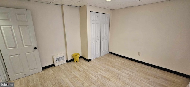 unfurnished bedroom featuring a paneled ceiling, light wood-type flooring, and a closet