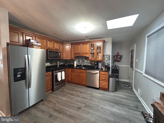 kitchen with appliances with stainless steel finishes, sink, light wood-type flooring, tasteful backsplash, and a skylight