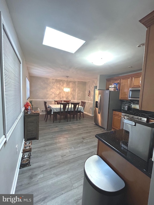 kitchen with stainless steel appliances, a skylight, dark stone counters, and light hardwood / wood-style floors