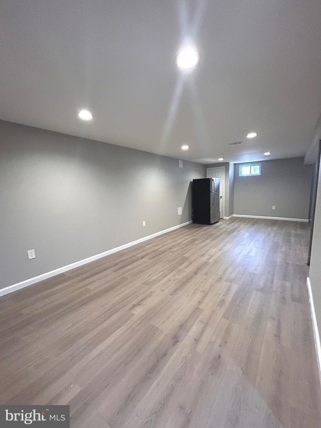 basement with light hardwood / wood-style floors and stainless steel fridge