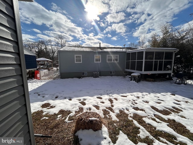 snow covered back of property with a sunroom