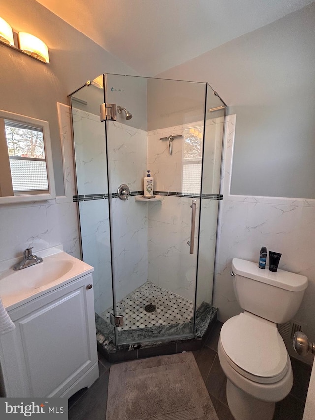 bathroom with walk in shower, toilet, vanity, and tile walls