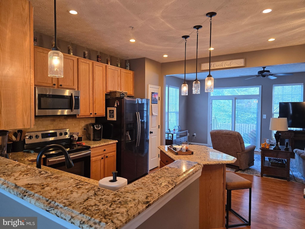 kitchen with decorative light fixtures, dark hardwood / wood-style flooring, stainless steel appliances, a kitchen breakfast bar, and light stone counters