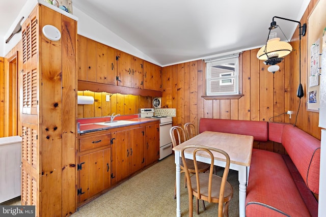 kitchen featuring lofted ceiling, wood walls, white electric stove, and sink