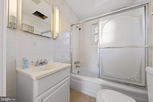 full bathroom featuring toilet, tile patterned floors, vanity, tile walls, and bath / shower combo with glass door