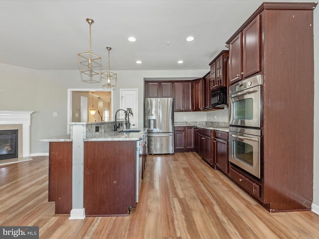 kitchen with hanging light fixtures, sink, a center island with sink, light hardwood / wood-style floors, and stainless steel appliances