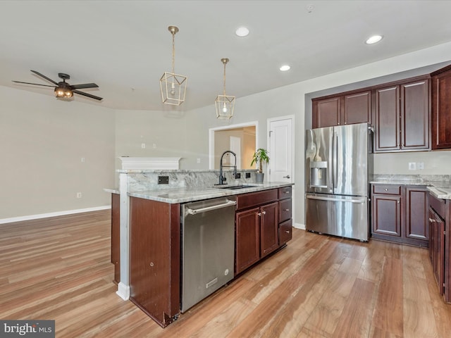 kitchen featuring light hardwood / wood-style floors, appliances with stainless steel finishes, light stone countertops, hanging light fixtures, and sink