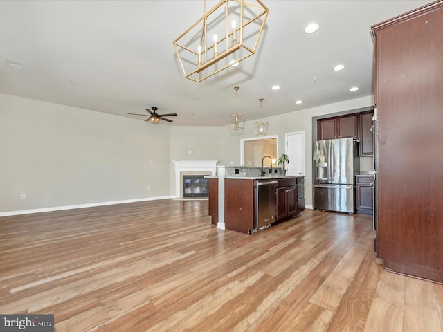 kitchen with appliances with stainless steel finishes, hanging light fixtures, light hardwood / wood-style flooring, ceiling fan, and a center island with sink