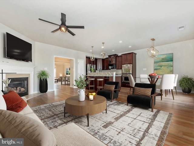 living room with ceiling fan with notable chandelier, sink, and light wood-type flooring